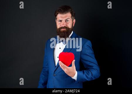 Trust me. Happy valentines day. Tuxedo man hold red heart. Love concept. Passionate mature lover hipster in formal suit. Businessman with bow tie. Romantic greeting. Fall in love. Celebrate love. Stock Photo