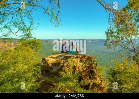 Unidentifiable couple sitting on a huge boulder and looking panoramic views from Baltzer Lookout in Blue Mountains National Park near Sydney in New Stock Photo