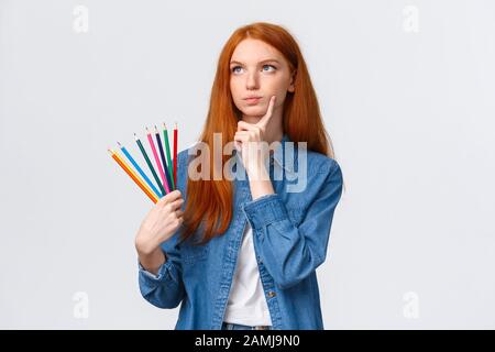 Thoughtful and focused, serious-looking determined redhead female student, teenager want draw something interesting, holding colored pencils look up Stock Photo