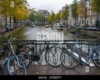 A bridge over a canal in the city of Amsterdam with bicycles chained to the railings. Stock Photo