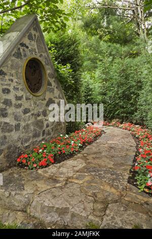 Flagstone path bordered by red and white Impatiens in private backyard formal garden in early summer. Stock Photo