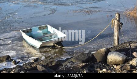 Small dinghy tied up to an icy shore in winter. Stock Photo