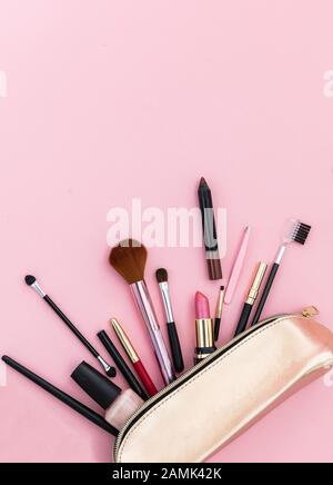 Make up cosmetic bag with professional accessories. Lipsticks and brushes in a gold cosmetic bag against pink color background, close up view, copy sp Stock Photo