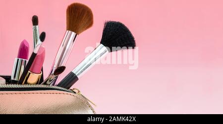 Make up cosmetic bag with professional accessories. Lipsticks and brushes in a gold cosmetic bag against pink color background, close up view, copy sp Stock Photo