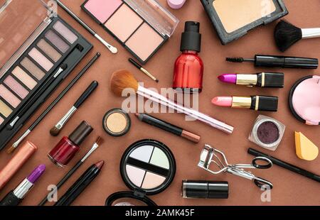 Make up cosmetics flat lay. Lipstick and nail polish, eye shadows and blush, brushes and pencils against brown  color background Stock Photo