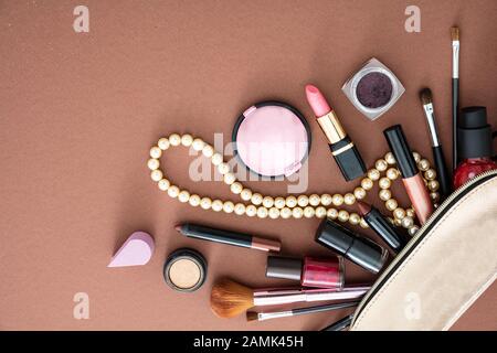 Make up cosmetic bag with professional accessories. Lipsticks and brushes out of a gold cosmetic bag against brown color background, copy space. Stock Photo