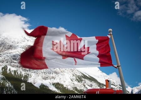 Canadian flag flying with blue sky and mountain in the background, on the boat to Spirit Island, Maligne Lake, Jasper National Park Stock Photo