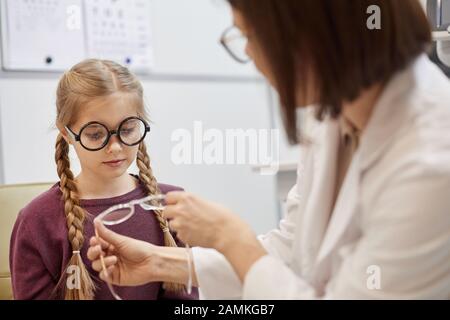 Portrait of cute teenage girl trying on glasses during vision test in modern ophthalmology clinic, copy space Stock Photo