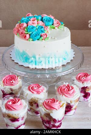 Festive cake with cream roses and multilayer dessert with fruit and cream cheese in a glass jar on a light background. Stock Photo