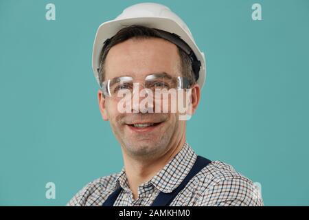 Head and shoulders portrait of professional worker or builder smiling at camera while posing confidently against blue background, copy space Stock Photo