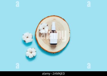 Zero waste concept. Glass reusable bottle for natural oil, perfume or dosodorant surrounded by cotton flowers on a wooden cut, tray. Stock Photo