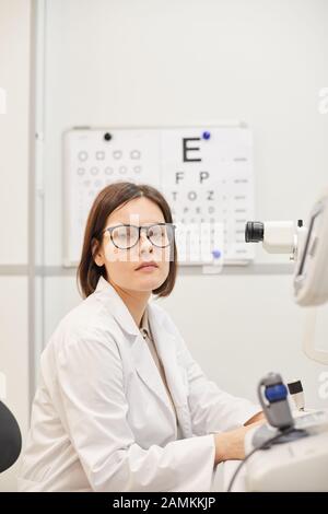 Portrait of young female ophthalmologist looking at camera while posing by refractometer machine in modern clinic, copy space Stock Photo