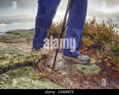 Woman legs in high waterproof boots make step over water pool on the rocky journey. Misty rainy weather in mountains Stock Photo