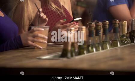 Women hanging out, having drink at bar counter, chatting online on smartphones Stock Photo