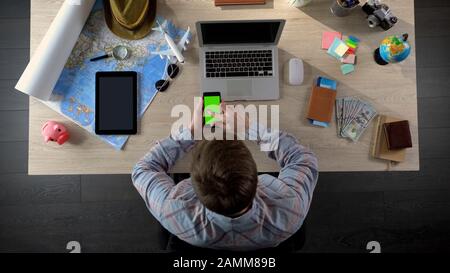 Man swiping pages on smartphone with green screen, using travel application Stock Photo