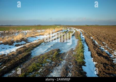 Muddy frozen rural road through fields, horizon and sky Stock Photo