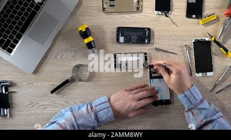 Repair specialists upgrading and maintaining gadgets, examining broken phones Stock Photo