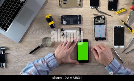 Male repairer turning on smartphone with green screen checking it after fixing Stock Photo