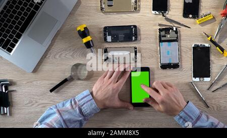 Repairer checking phone functionality after fixing, smartphone with green screen Stock Photo