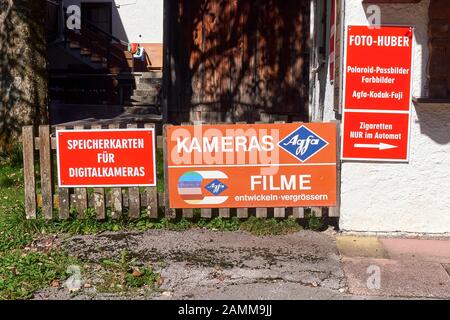 old faded advertising sign for Agfa film processing, next to a new board with the text Memory cards for digital cameras, Bayrischzell, 29.09.2016 [automated translation] Stock Photo