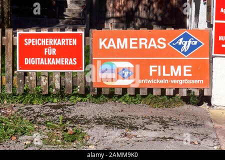 old faded advertising sign for Agfa film development, next to a new board with the text Memory cards for digital cameras, Bayrischzell, 29.09.2016 [automated translation] Stock Photo