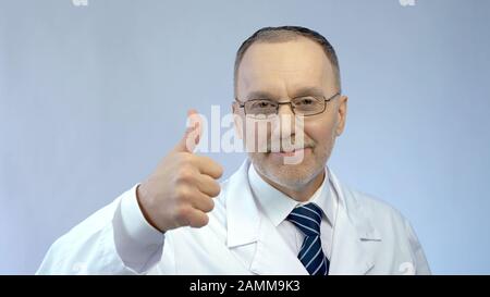Male doctor smiling at camera, making thumbs-up hand sign, best medical aid Stock Photo