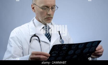 Experienced male therapist looking at patients brain scan, checking MRI results Stock Photo