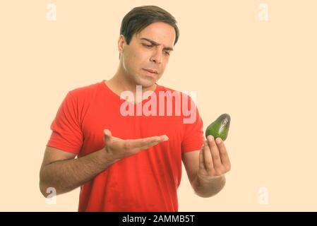 Studio shot of young Persian man looking and pointing at avocado isolated against white background Stock Photo