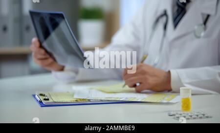 Therapist analyzing patient lungs x-ray to write down diagnosis, treatment Stock Photo