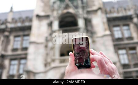 On Munich's Marienplatz, a tourist photographs the carillon in the town hall tower with his smartphone. [automated translation] Stock Photo