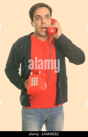 Thoughtful young Persian man standing and talking on old telephone while looking shocked Stock Photo