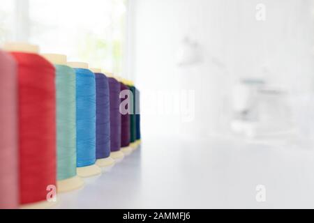 Row of multicolored spools of sewing threads on a white table. Workplace of seamstress. Sewing background with copy space. Stock Photo