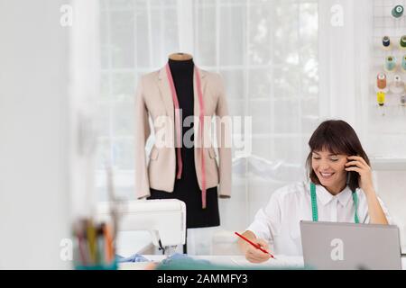 Young female dressmaker working in sewing studio. Businesswoman talking on the phone with a client. Bespoke tailoring. Private enterprise. Hobby and Stock Photo