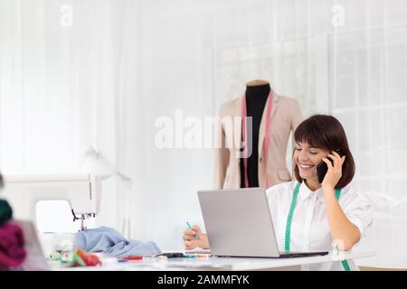 Young female dressmaker working in sewing studio. Businesswoman talking on the phone with a client. Bespoke tailoring. Private enterprise. Hobby and Stock Photo