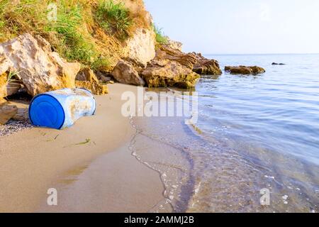 Used blue plastic drums for storing water and other liquids is washed up by the sea on sandy beach, waste. Stock Photo