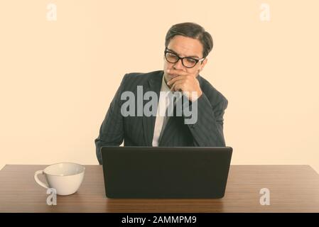 Persian businessman wearing eyeglasses while thinking and using laptop on wooden table Stock Photo