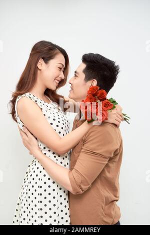 Young man with bouquet of flowers hugging his girlfriend on white background Stock Photo
