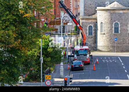 Construction workers build scaffold tower via height hoist for building. People loading scaffold using cherry picker wearing hard hats. Dublin Ireland Stock Photo