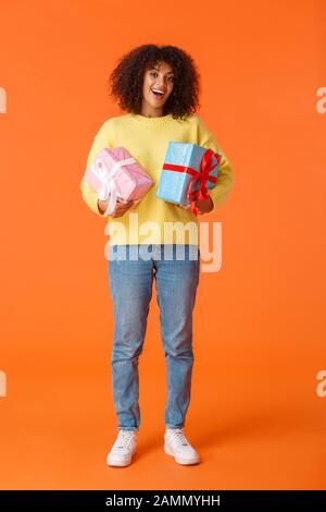Full-length vertical shot excited cute happy african-american female received gifts for holidays, standing amused and delighted, holding two wrapped Stock Photo