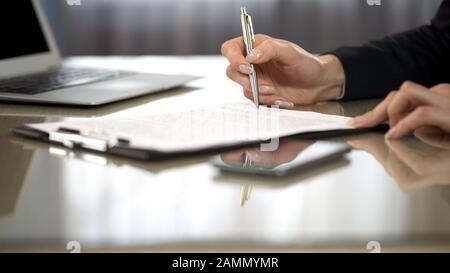 Woman in suit reading terms and conditions of agreement, signing contract Stock Photo
