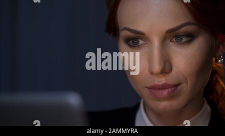 Beautiful business lady working on laptop, looking on screen at night office Stock Photo