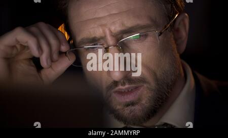 Detective sitting at laptop at night office, thinking about complicated case Stock Photo