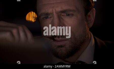 Professional detective working on laptop at night, holding eyeglasses in hand Stock Photo