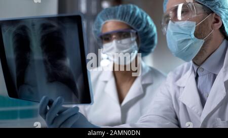 Doctors studying x-ray of lungs in lab, analyzing and discussing diagnosis Stock Photo