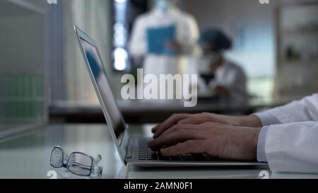 Scientist typing experiment results on laptop, working at project in laboratory Stock Photo