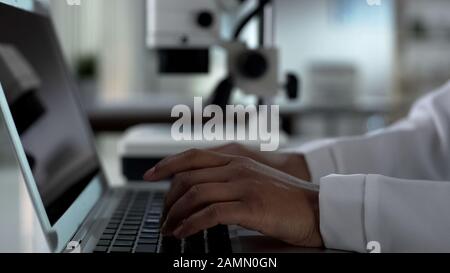 Female scientist hands typing on laptop, working on experimental research in lab Stock Photo