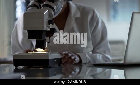 Female researcher looking at test sample under microscope, working in clinic Stock Photo