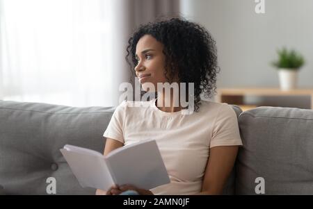African woman distracted from reading looks out the window Stock Photo