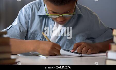 First-grader boy carefully writing letters in his copybook, doing homework Stock Photo