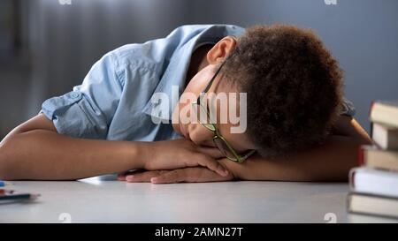 Tired pupil sleeping, sitting at desk, hard educational process, overworked boy Stock Photo